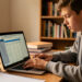 Un lycéen consulte ses résultats sur un ordinateur portable dans une salle d’étude, éclairage chaleureux, ambiance calme et documentaire.