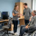 Une formatrice accueille chaleureusement un homme adulte en situation de handicap dans une salle de formation accessible équipée d’une rampe et d’un ordinateur adapté.